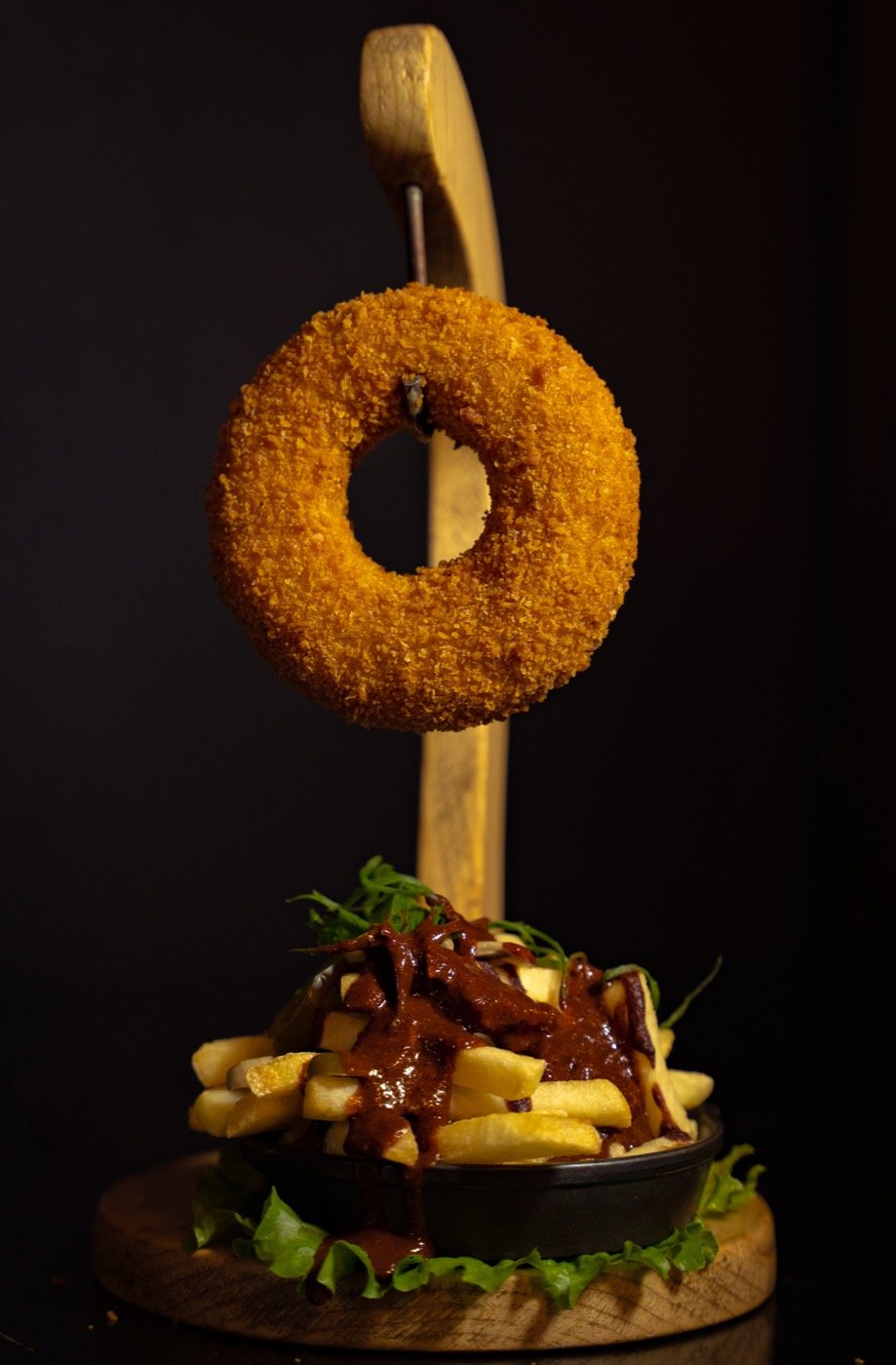 Cheese-filled donut hanging over a bowl of chilli fries