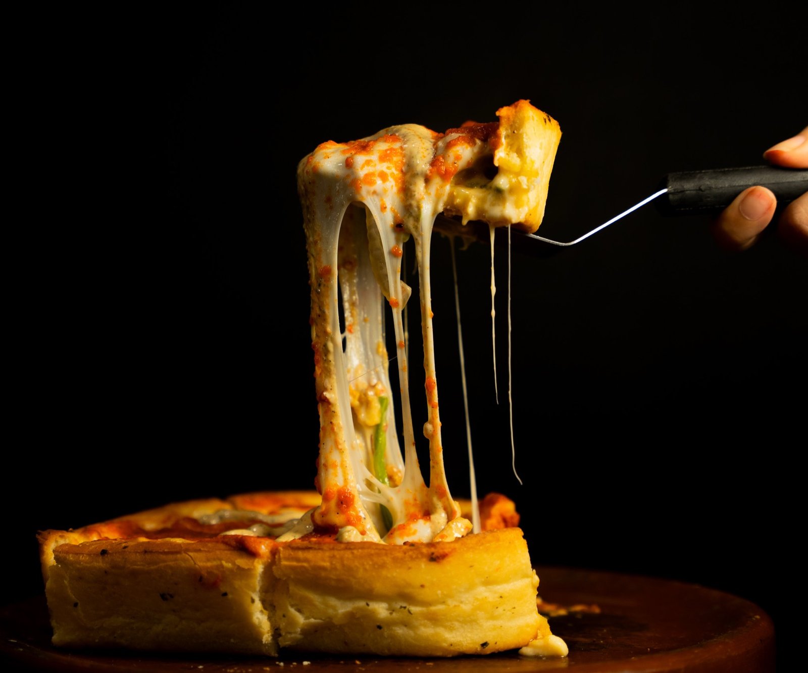 A slice of deep dish pizza stretching melted cheese as it is lifted